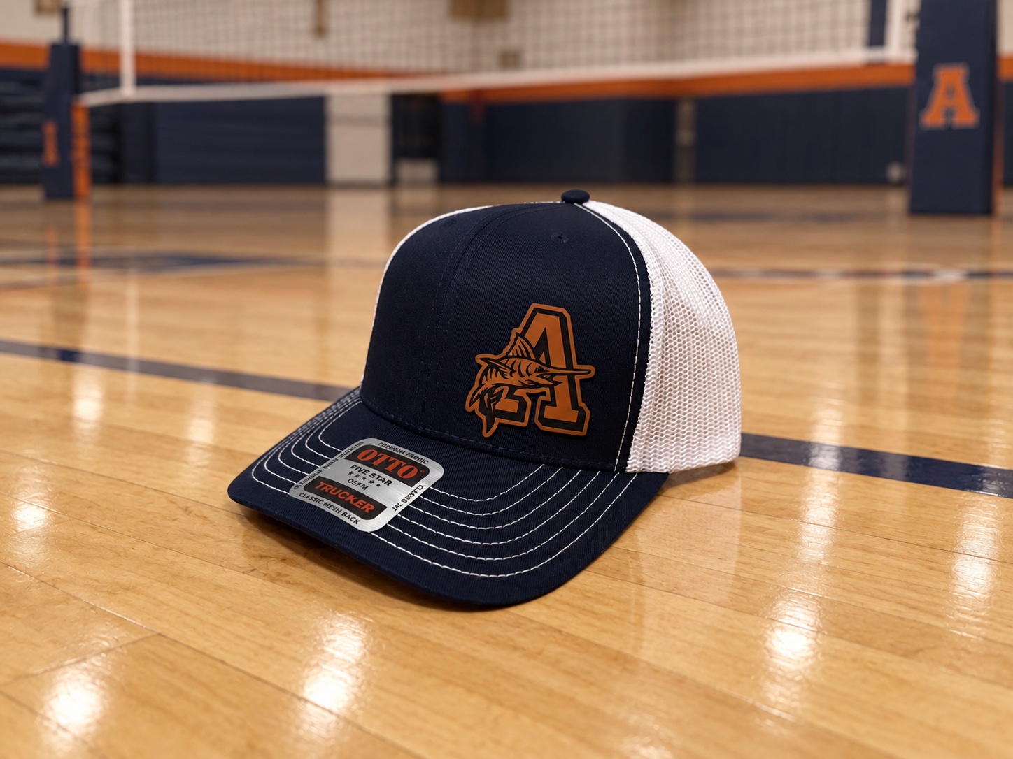 Navy and white mesh Arnold High School trucker hat with an orange A and marlin patch on an indoor volleyball court.