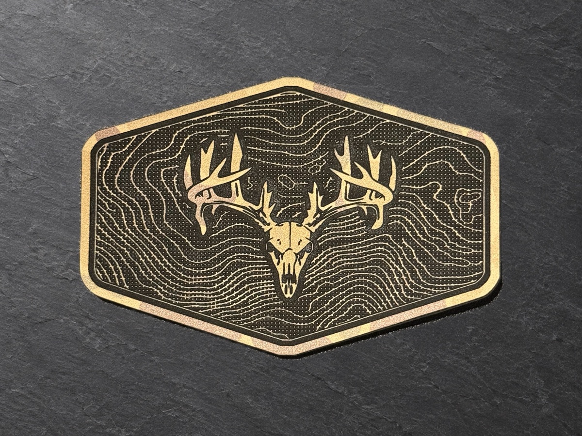 Antler and topographic engraving on a hexagonal patch, photographed against slate